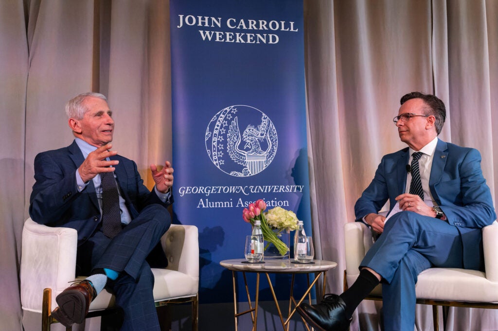 two men sit in chairs on a stage